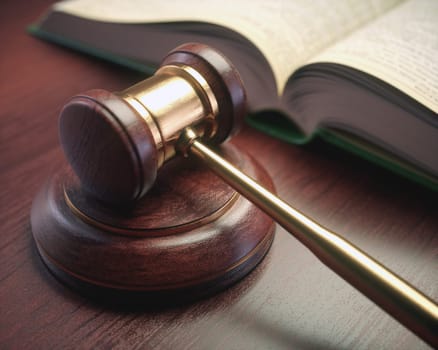 Wooden judge hammer with golden details and a legislation book beside.