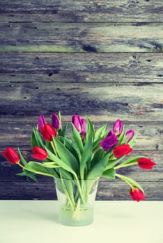 bouquet of red and violet tulips  in vase in front of wooden background