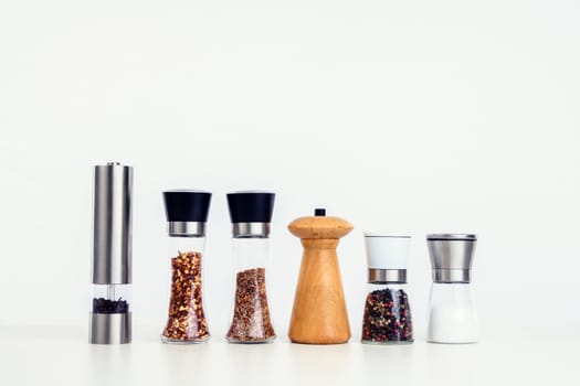 different spice mills with salt,pepper and other herbs in front of white background