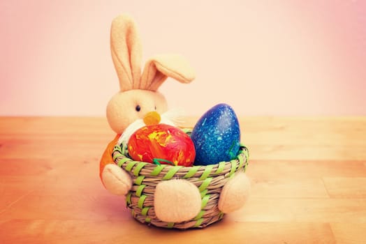 easter bunny in basket with egg in front of pink background