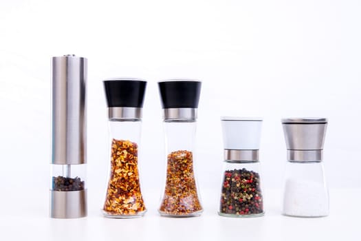 different spice mills with salt,pepper and other herbs in front of white background