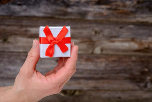 womans hand hold little gift box in front of wooden background