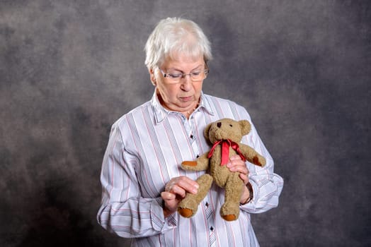 gray haired grandmother with stethoscope is puppet doctor for teddy bear