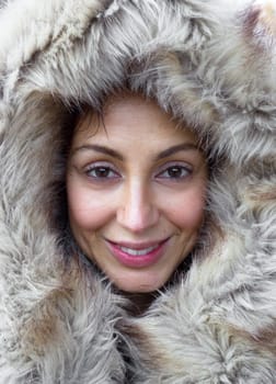 Portrait of cheerful and smiling girl  his face is framed by a fur hood. The make up is natural.