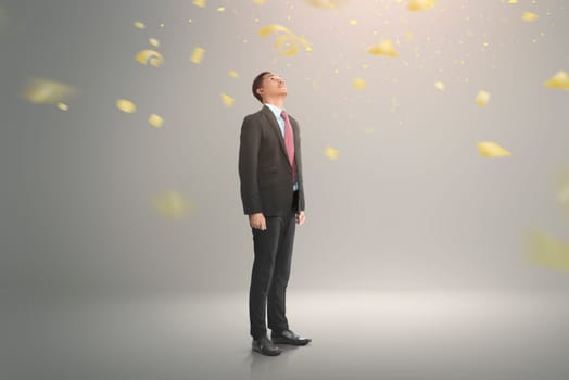 Young asian businessman looking up with falling confetti on gray background