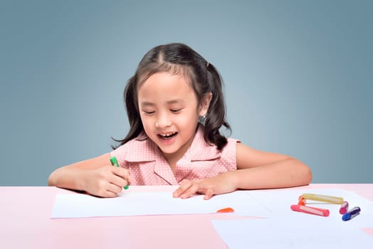 Beautiful asian little girl drawing with wax crayons over gray background