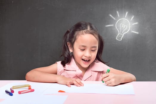 Cheerful asian little girl having new idea for drawing with crayon on black background