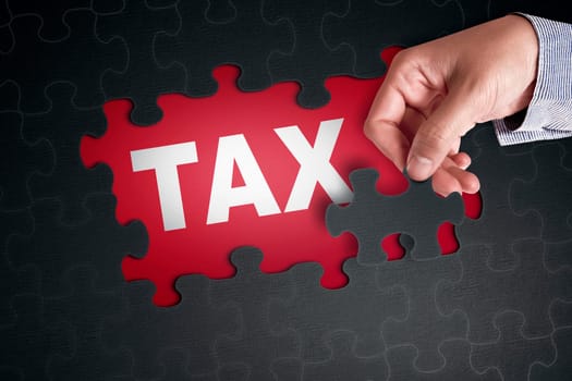 People hand placing puzzle piece with word TAX on red background