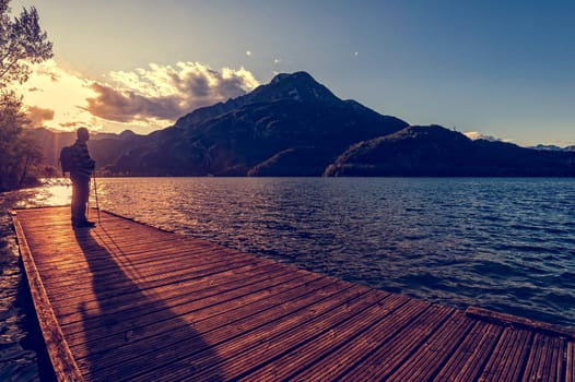 Hiker standing on dock end on lake. Tramper looking sunset over the lake.