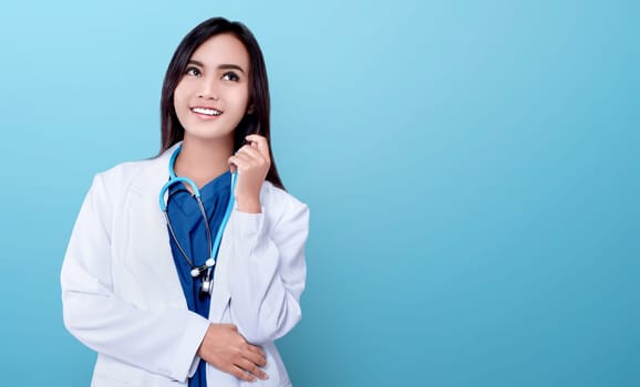 Young asian doctor woman in white coat and stethoscope over blue bright background