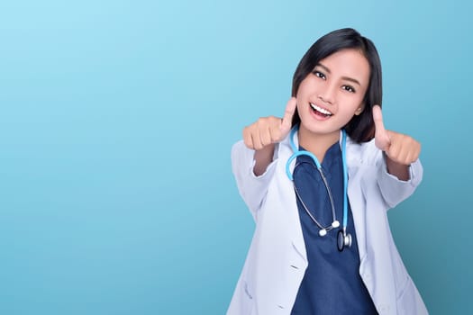 Happy asian woman doctor giving thumbs up over blue background