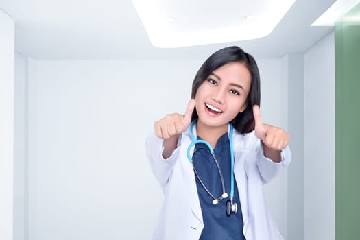 Beautiful asian female doctor in white coat showing thumbs up at clinic room