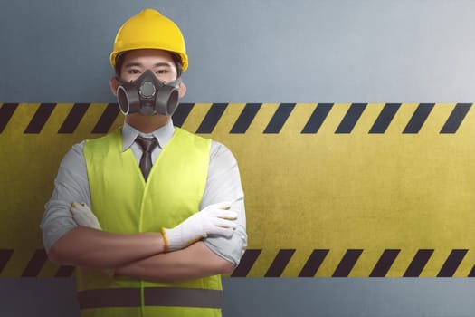 Young asian construction worker with crossed arm standing against yellow striped on the wall