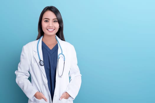 Smiling asian woman physician in a white coat over blue background