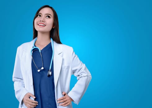 Young asian female doctor in white coat looking up with blue background
