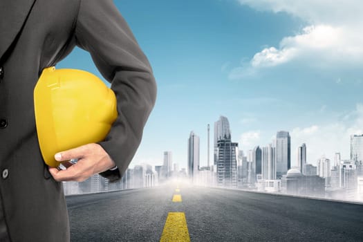Construction worker holding yellow helmet with city background