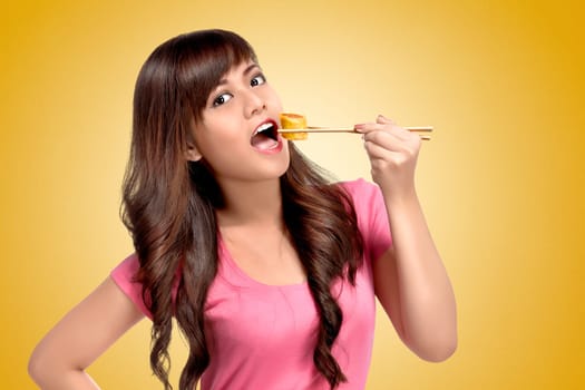 Young asian woman eating sushie with chopsticks over yellow background