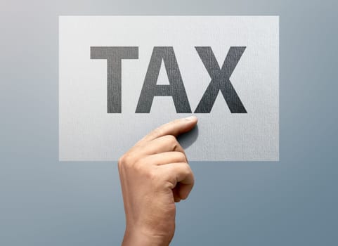 People hands holding white paper with TAX text over grey background