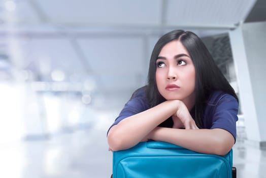 Bored asian traveler woman with suitcase waiting for her flight on airport terminal