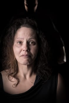 Abused woman victim of domestic violence, with husband silhouette in the background