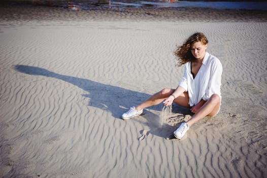 lovely young woman with curly hair, the romance of youth, a journey walk on a warm summer sunny day on a sandy beach with water