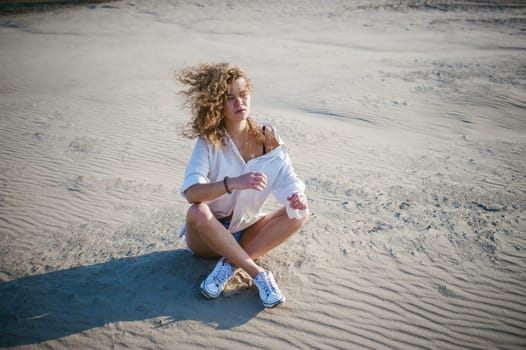 lovely young woman with curly hair, the romance of youth, a journey walk on a warm summer sunny day on a sandy beach with water