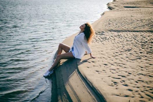 lovely young woman with curly hair, the romance of youth, a journey walk on a warm summer sunny day on a sandy beach with water