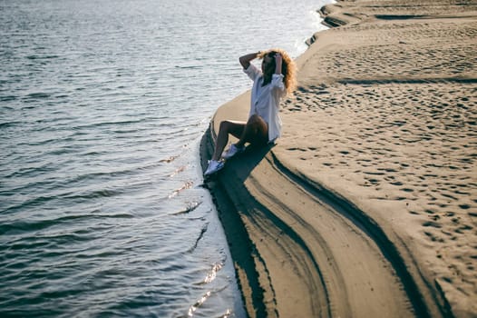 lovely young woman with curly hair, the romance of youth, a journey walk on a warm summer sunny day on a sandy beach with water