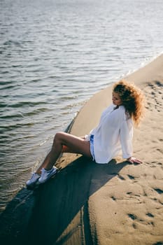 lovely young woman with curly hair, the romance of youth, a journey walk on a warm summer sunny day on a sandy beach with water