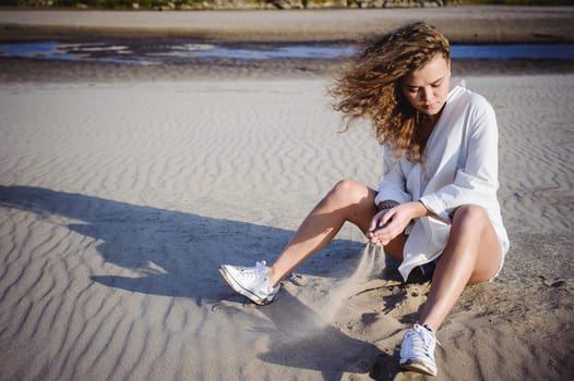 lovely young woman with curly hair, the romance of youth, a journey walk on a warm summer sunny day on a sandy beach with water