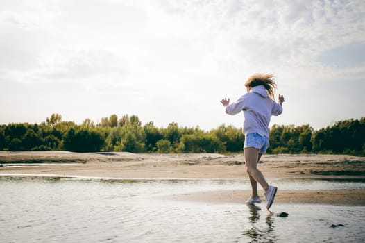lovely young woman with curly hair, the romance of youth, a journey walk on a warm summer sunny day on a sandy beach with water