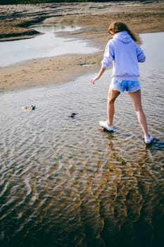 lovely young woman with curly hair, the romance of youth, a journey walk on a warm summer sunny day on a sandy beach with water