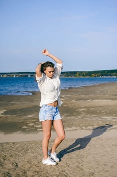 lovely young woman with curly hair, the romance of youth, a journey walk on a warm summer sunny day on a sandy beach with water