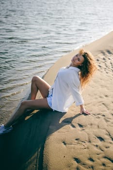 lovely young woman with curly hair, the romance of youth, a journey walk on a warm summer sunny day on a sandy beach with water
