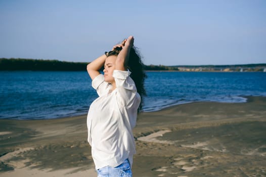 lovely young woman with curly hair, the romance of youth, a journey walk on a warm summer sunny day on a sandy beach with water