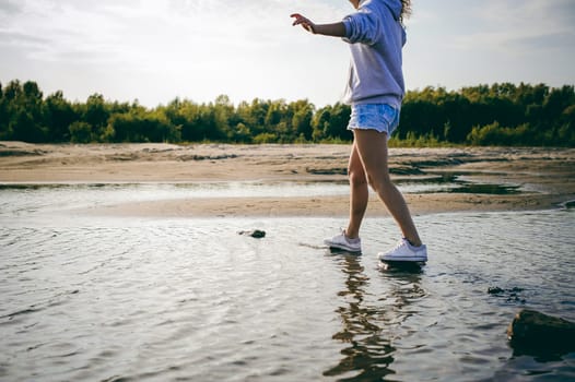 lovely young woman with curly hair, the romance of youth, a journey walk on a warm summer sunny day on a sandy beach with water