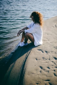 lovely young woman with curly hair, the romance of youth, a journey walk on a warm summer sunny day on a sandy beach with water