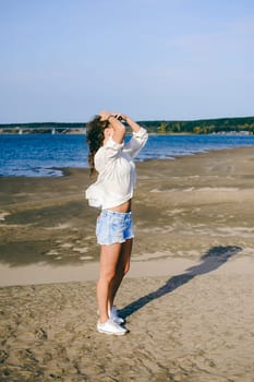 lovely young woman with curly hair, the romance of youth, a journey walk on a warm summer sunny day on a sandy beach with water
