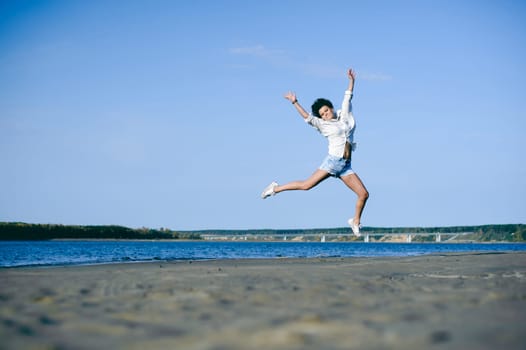 lovely young woman with curly hair, the romance of youth, a journey walk on a warm summer sunny day on a sandy beach with water