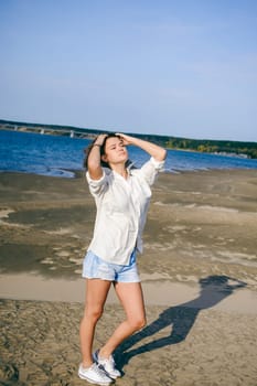 lovely young woman with curly hair, the romance of youth, a journey walk on a warm summer sunny day on a sandy beach with water