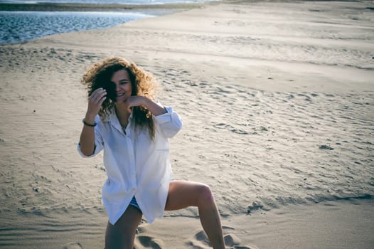 lovely young woman with curly hair, the romance of youth, a journey walk on a warm summer sunny day on a sandy beach with water