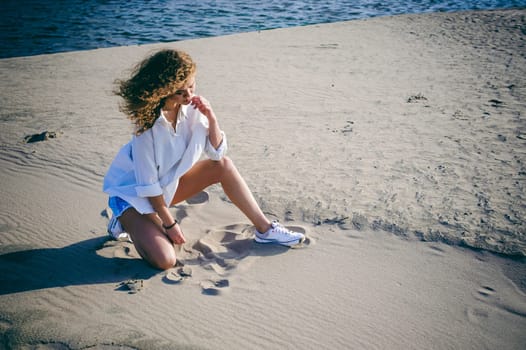 lovely young woman with curly hair, the romance of youth, a journey walk on a warm summer sunny day on a sandy beach with water