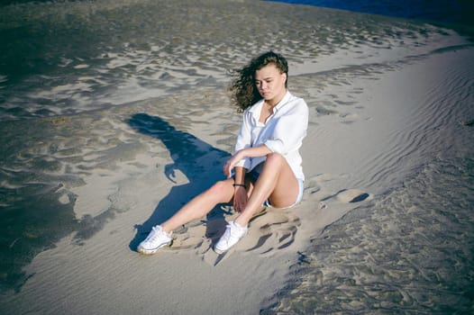 lovely young woman with curly hair, the romance of youth, a journey walk on a warm summer sunny day on a sandy beach with water