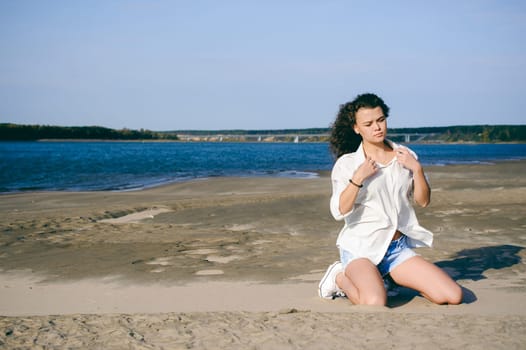 lovely young woman with curly hair, the romance of youth, a journey walk on a warm summer sunny day on a sandy beach with water