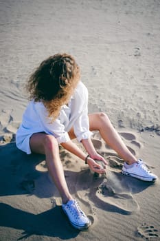 lovely young woman with curly hair, the romance of youth, a journey walk on a warm summer sunny day on a sandy beach with water