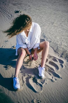 lovely young woman with curly hair, the romance of youth, a journey walk on a warm summer sunny day on a sandy beach with water