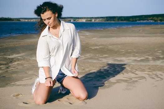 lovely young woman with curly hair, the romance of youth, a journey walk on a warm summer sunny day on a sandy beach with water