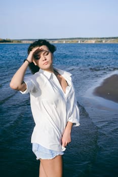 lovely young woman with curly hair, the romance of youth, a journey walk on a warm summer sunny day on a sandy beach with water