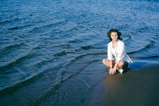 lovely young woman with curly hair, the romance of youth, a journey walk on a warm summer sunny day on a sandy beach with water