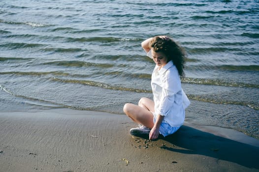 lovely young woman with curly hair, the romance of youth, a journey walk on a warm summer sunny day on a sandy beach with water